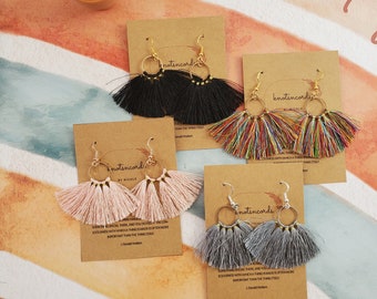 May include: Four pairs of handmade tassel earrings with gold hoops. The tassels are in black, rainbow, pink, and grey.