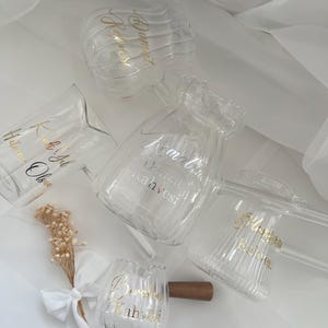 Op de afbeelding: Een collectie van heldere glazen vaten met verticale ribbels en gouden letters. De items omvatten een kan, mokken en kleine kopjes met diverse Turkse inscripties. Een klein boeket gedroogde bloemen met een wit lint is inbegrepen.