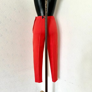 May include: A pair of red, straight-leg pants with a center crease. The pants are on a mannequin and are hanging on a white wall.