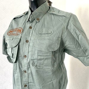 Pu&ograve; includere: Una camicia verde a maniche corte con bottoni, pi&ugrave; tasche e una toppa ricamata marrone che dice "African Wildlife Safaris" sul petto sinistro.