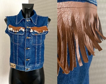 May include: A blue denim vest with brown leather fringe trim and a white label that says "Lois" on the front.