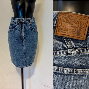 Può includere: Gonna di jeans blu con effetto stone-washed. La gonna ha vita alta, tasche e un classico design a cinque tasche. L'etichetta recita "FRISCO HIGHLIFE JEANS".