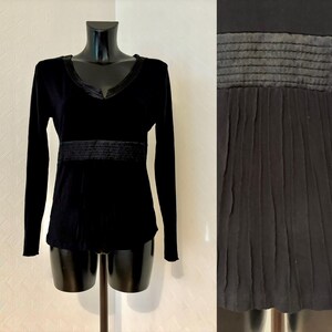 May include: Black long-sleeved shirt with a V-neck and a black band around the waist. The shirt has a slightly gathered look at the bottom.
