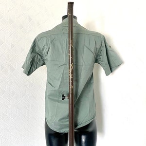Pu&ograve; includere: Una camicia verde salvia a maniche corte con bottoni su un manichino.
