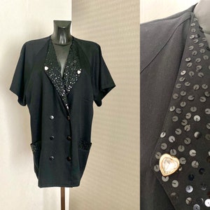 May include: A black blazer with a double-breasted closure and short sleeves. The collar and pockets are trimmed with black sequins. A rhinestone heart pin is attached to the collar.