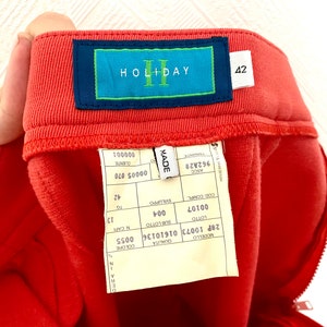 May include: A red pair of pants with a label that says "HOLIDAY" and "42". The label also has the words "MADE", "ASCO", "962A28", "LOTTO", "00107", "004", "COD.COMPLE", "SVILUPPO", "16", "42", "CUENTE", "00005 070", "000001", "QUALITA", "COLORE", "28P 10073 01610136 0055", "MOUELLO".