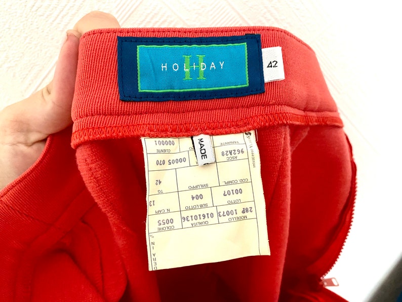 May include: A red pair of pants with a label that says "HOLIDAY" and "42". The label also has the words "MADE", "ASCO", "962A28", "LOTTO", "00107", "004", "COD.COMPLE", "SVILUPPO", "16", "42", "CUENTE", "00005 070", "000001", "QUALITA", "COLORE", "28P 10073 01610136 0055", "MOUELLO".