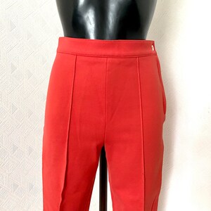 May include: A pair of red pants with a straight leg and a button closure. The pants are made of a smooth, lightweight fabric.