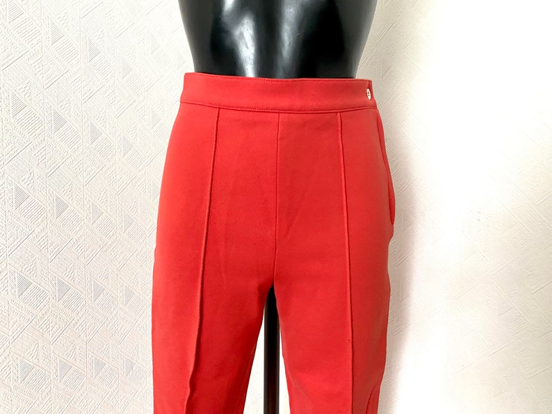 May include: A pair of red pants with a straight leg and a button closure. The pants are made of a smooth, lightweight fabric.
