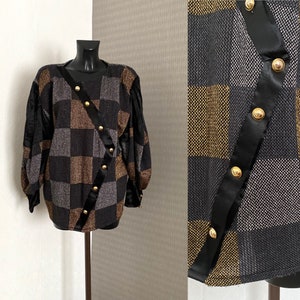 Peut inclure: Un pull à carreaux noir et or avec une bordure en satin noir et des boutons dorés. Le pull a une coupe ample et des manches longues.