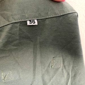 Pu&ograve; includere: Una giacca utility verde con un'etichetta di taglia che dice "36".