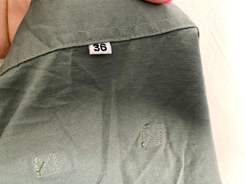 Pu&ograve; includere: Una giacca utility verde con un'etichetta di taglia che dice "36".