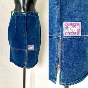 May include: A blue denim skirt with a front zipper and a green waistband. The skirt has two patches with colorful designs, one that says "Summer Fun" and the other with a cartoon ice cream cone and beach chair.