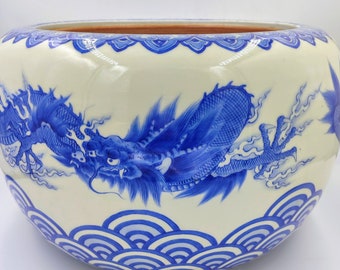 Puede incluir: Un gran cuenco de cerámica blanca con un diseño de dragón azul y blanco. El cuenco tiene un borde festoneado y un patrón de ondas azul y blanco alrededor de la base.