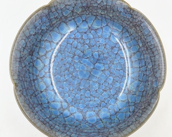 May include: A blue ceramic bowl with a crackled glaze. The bowl has a scalloped rim and a deep, round shape.