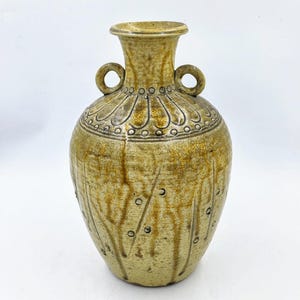 May include: A decorative, antique-style vase with a textured, aged appearance. The vase is primarily a muted yellow-green color with darker brown accents and a crackled finish. It features two small handles and a detailed, patterned band around the neck.