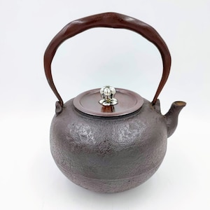 May include: A dark brown cast iron teapot with a wooden handle and a silver knob on the lid.