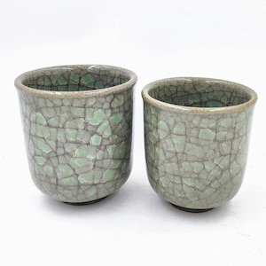 May include: Two green ceramic teacups with a crackle glaze. The cups have a light green base and a darker green crackle glaze.