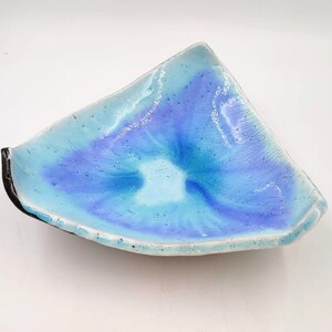 May include: A light blue ceramic dish with a white and purple swirl design. The dish has a slightly irregular shape and a textured surface.