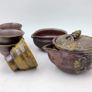 以下が含まれることがあります： 茶器セット。茶器は、茶色と金色で、茶壺、蓋、茶碗4つがあります。茶壺は、ユニークな取っ手と斑点模様の釉薬が施されています。