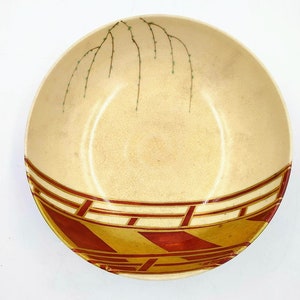 Puede incluir: Un cuenco grande, redondo, de cerámica de color crema con un diseño geométrico rojo y dorado alrededor del borde. El cuenco tiene un diseño de sauce llorón verde pintado en el interior.