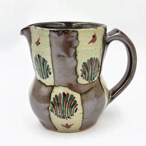 May include: A brown ceramic pitcher with a handle. The pitcher has a geometric pattern of green, red, and white on a brown background.
