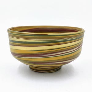 May include: A small, round bowl with a swirling pattern of yellow, red, green, and white stripes. The bowl is made of ceramic and has a glossy finish.