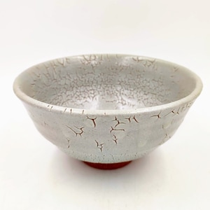 May include: A white ceramic bowl with a crackled glaze. The bowl has a rounded shape and a slightly flared rim.