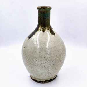 May include: A white ceramic vase with a round body and a narrow neck. The vase has a brown and green glaze with a speckled texture.