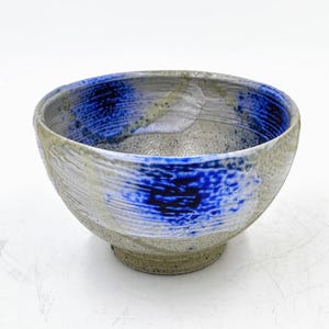May include: A white ceramic bowl with blue and gray glaze. The bowl has a rounded shape and a slightly flared rim.