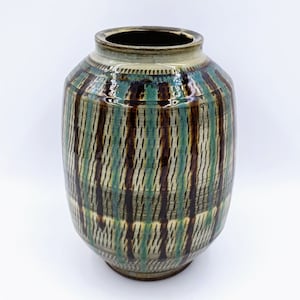 Puede incluir: Un jarrón de cerámica con un patrón de rayas marrones, verdes y blancas. El jarrón tiene un cuerpo redondeado y una abertura ligeramente acampanada.