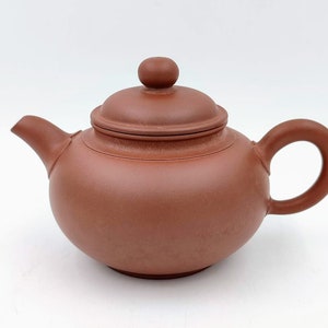 May include: A small, reddish-brown clay teapot with a rounded body and a lid with a knob on top. The teapot has a short spout and a curved handle.