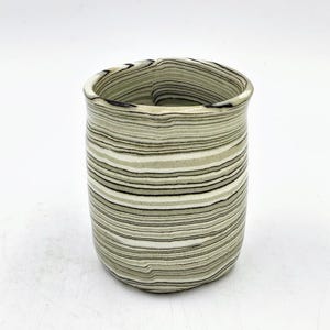 May include: A white ceramic cup with black and gray stripes. The cup is cylindrical and has a smooth, rounded rim.
