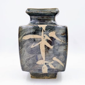 May include: A square ceramic vase with a dark blue glaze and white brushstrokes. The vase has a wide mouth and a narrow base.