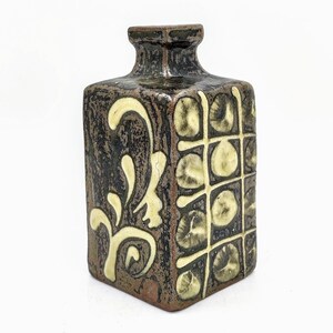 May include: A square ceramic vase with a brown glaze and white geometric and floral designs.