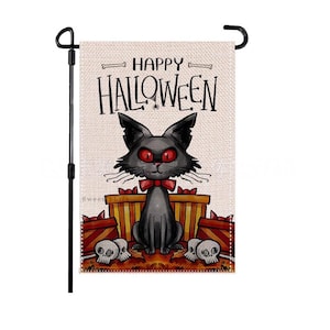 Puede incluir: Una bandera de jardín rectangular que muestra un gato negro con ojos rojos y una pajarita roja, sentado frente a cajas de regalo naranjas y amarillas y dos calaveras. El texto HAPPY HALLOWEEN está impreso en negro arriba, flanqueado por dos huesos.