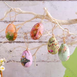 May include: Five wooden Easter eggs with different floral and animal designs hanging from a white branch. The eggs are decorated with pink, green, and orange colors.