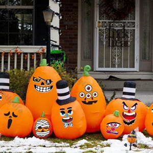 Puede incluir: Una colección de calabazas inflables de color naranja con varias caras y expresiones de dibujos animados, algunas con sombreros. Las calabazas están decoradas con pegatinas y se colocan al aire libre para Halloween.