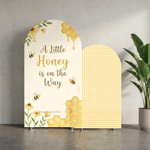 May include: Two arched backdrop covers featuring a cream background with watercolour illustrations of bees, honeycombs, and yellow flowers. The text reads A Little Honey is on the Way in brown script. One panel has a yellow and white gingham check pattern.