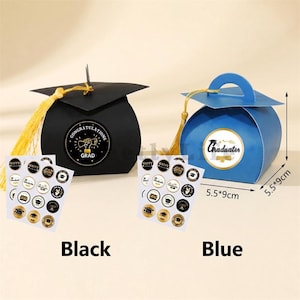 May include: Black and blue graduation-themed gift boxes shaped like mortarboards, each with a tassel. The black box has a "Congratulations Grad" sticker, and the blue box has a "Graduates" sticker. Each box is 5.5 x 9 inches.