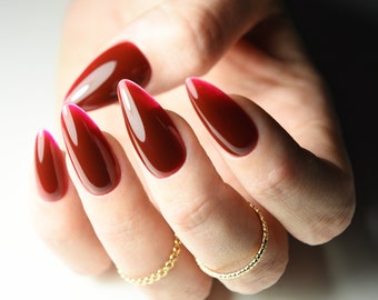 May include: Close-up of a hand with long, almond-shaped nails painted a deep red with a gradient effect. The nails are polished to a high shine.