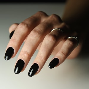 Puede incluir: Primer plano de una mano con cuatro uñas ovaladas pintadas de negro.