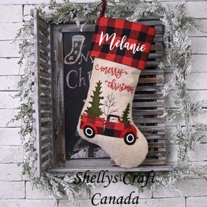 May include: A personalised Christmas stocking with a red and black buffalo plaid cuff. The stocking features a red truck with a Christmas tree in the back, and the text "merry christmas" is embroidered on the stocking. The stocking is personalised with the name "Melanie".