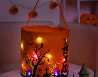 May include: Orange Halloween trick-or-treat bag with a black and white spooky design and built-in LED lights. The bag has a handle and is shaped like a bucket.