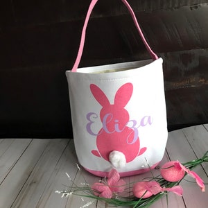 Puede incluir: Bolsa de lona rosa en forma de conejo de Pascua con una cola de algod&oacute;n blanca y el nombre "Eliza" impreso en morado.
