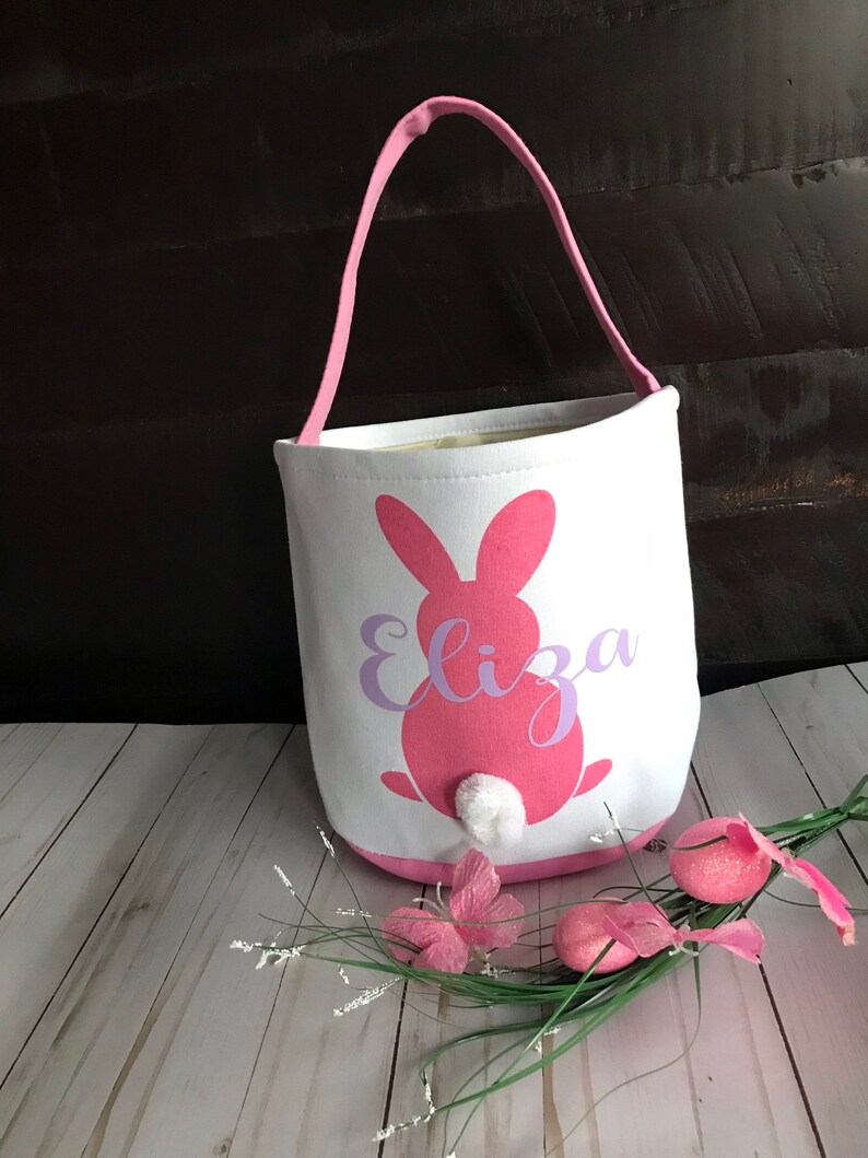 Puede incluir: Bolsa de lona rosa en forma de conejo de Pascua con una cola de algod&oacute;n blanca y el nombre "Eliza" impreso en morado.