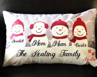 May include: A white pillow with a winter theme featuring four snowmen with red hats and scarves. The snowmen are labeled "Scarlett", "Mom", "Mum", and "Curtis". The pillow also has the text "The Keating Family" and "Koda" in red.