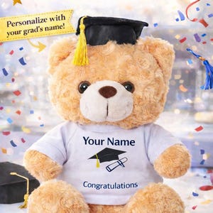 May include: A soft teddy bear wearing a graduation cap and a white t-shirt. The shirt has the text "Your Name" above a graduation cap graphic and the word "Congratulations". The image includes the text "For your 2026 GRADUATE!"