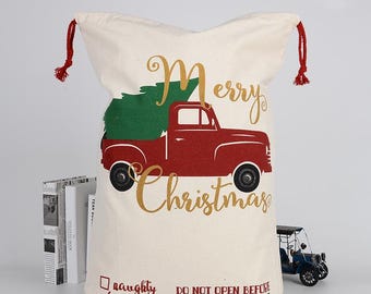 May include: A white canvas Christmas gift bag with a red truck carrying a Christmas tree. The bag has the text "Merry Christmas" and a checkbox to mark "naughty" or "nice". The bag also says "Do not open before December 25".