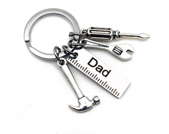 May include: Silver keychain with a ruler charm, a hammer charm, a wrench charm, and a screwdriver charm. The ruler charm has the word "Dad" engraved on it.